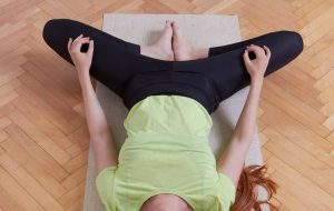 Woman does goddess pose on floor inside